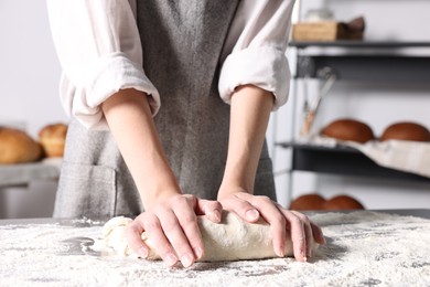 Woman kneading dough at table in kitchen, closeup