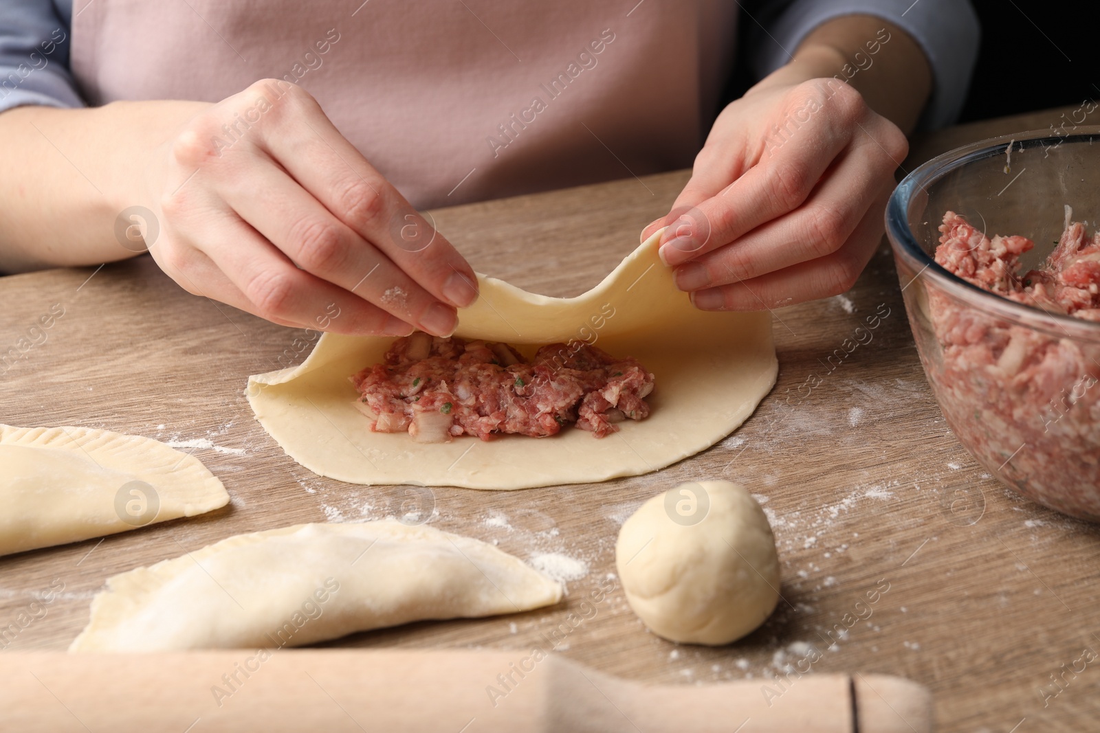 Photo of Woman making chebureki at wooden table, closeup