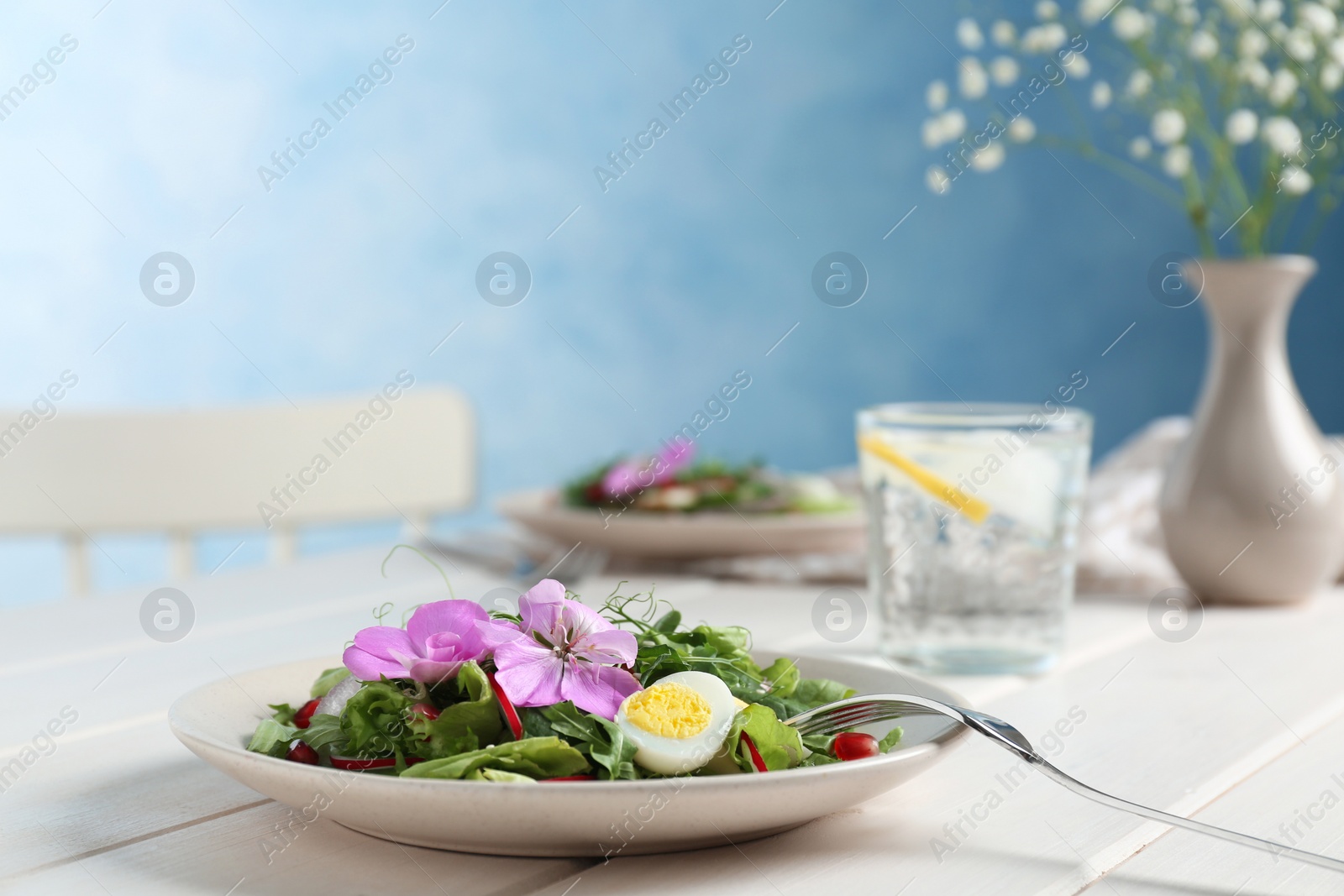 Photo of Fresh spring salad with flowers served on white wooden table