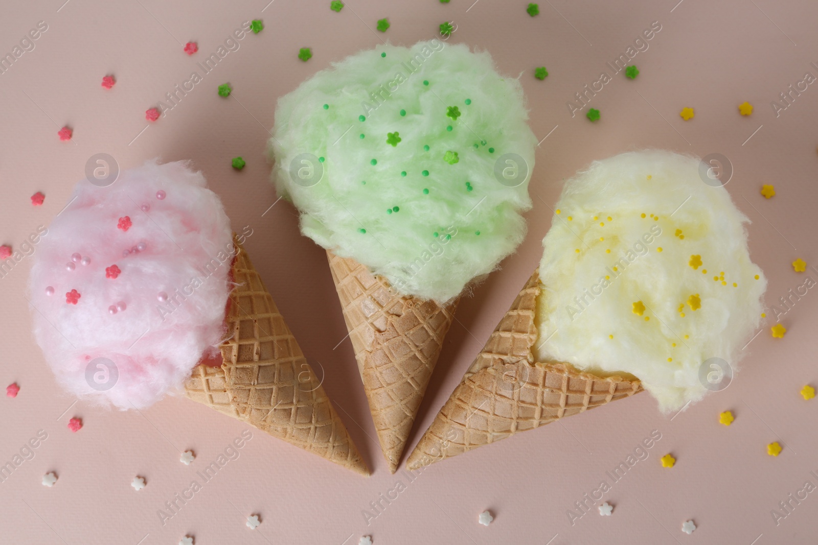 Photo of Sweet cotton candies in waffle cones on beige background, flat lay