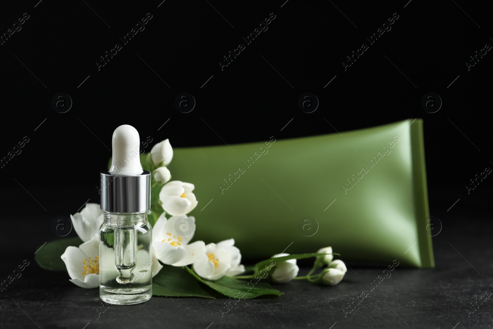 Photo of Cosmetic products and flowers on grey stone table against black background