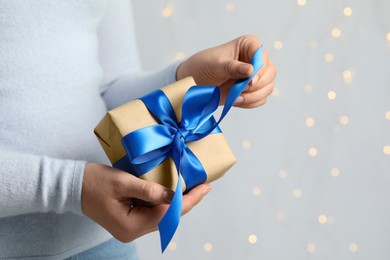 Photo of Woman holding gift box with blue bow against blurred festive lights, closeup and space for text. Bokeh effect
