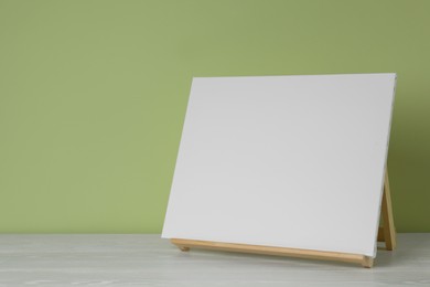 Photo of Wooden easel with blank canvas on white table. Space for text