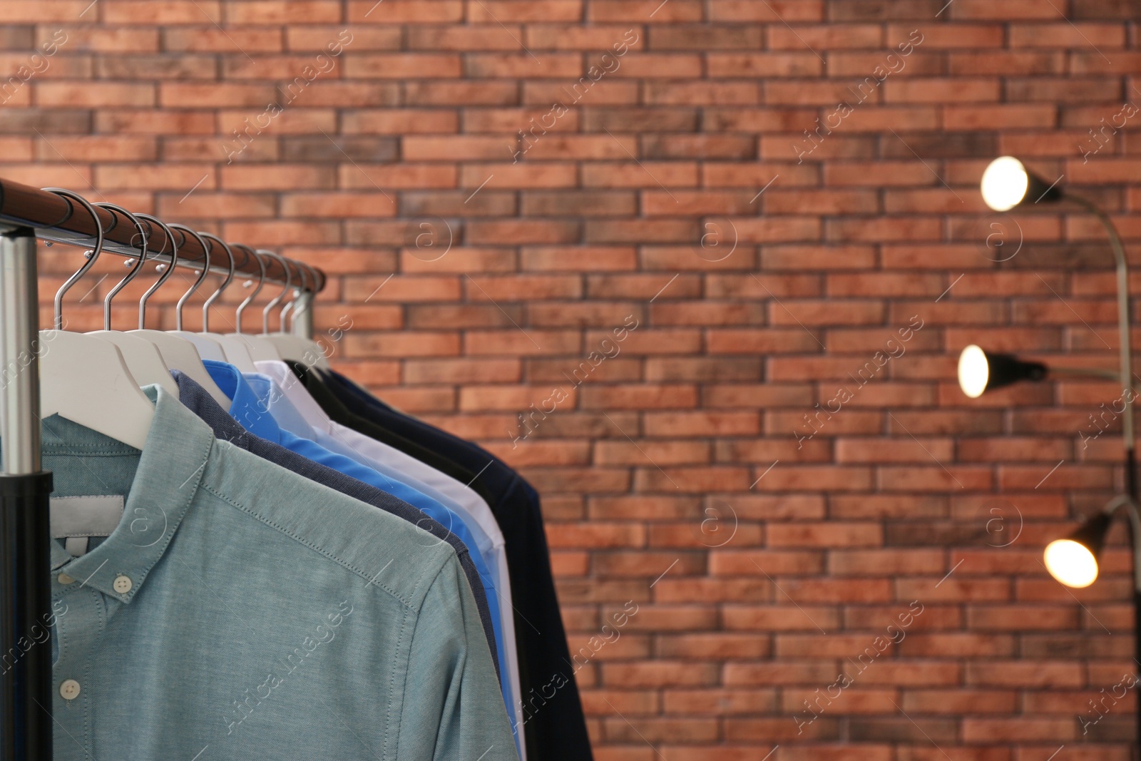 Photo of Wardrobe rack with stylish clothes near brick wall. Space for text