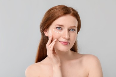 Photo of Beautiful woman with freckles and cream on her face against grey background