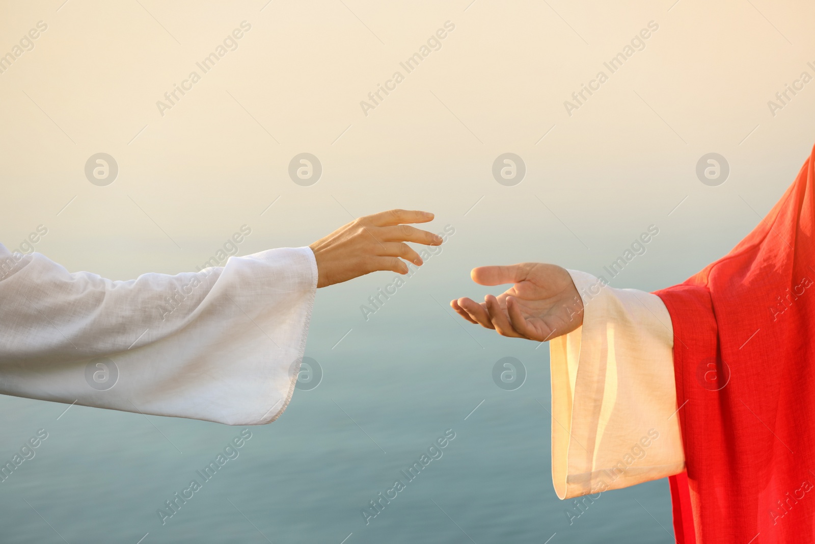 Photo of Woman reaching for Jesus Christ's hand near water outdoors, closeup