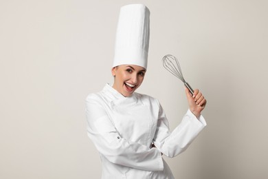 Photo of Happy professional confectioner in uniform holding whisk on light grey background
