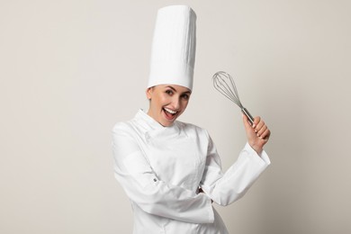 Happy professional confectioner in uniform holding whisk on light grey background