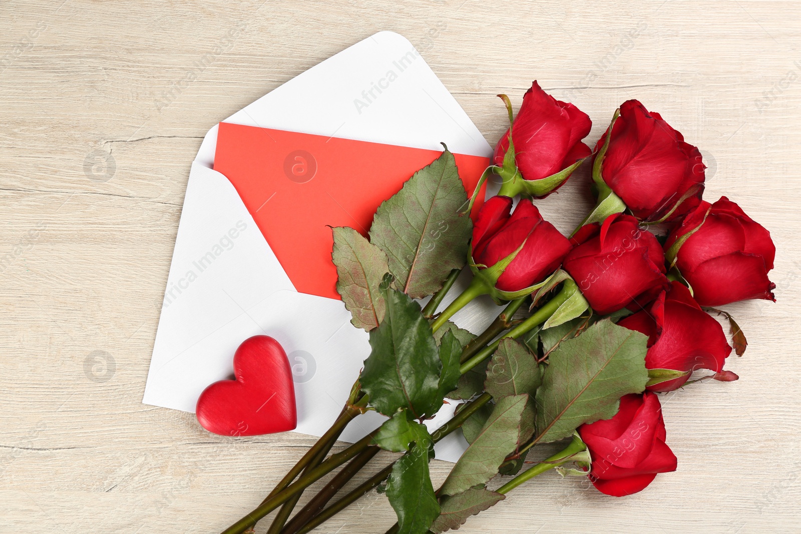 Photo of Beautiful red roses, envelope with love letter and decorative heart on white wooden background, flat lay. Valentine's Day celebration