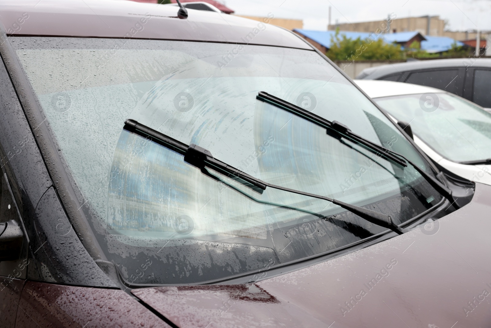 Photo of Car wipers cleaning water drops from windshield glass outdoors, closeup