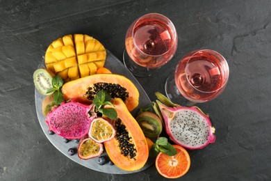 Photo of Delicious exotic fruits and wine on black table, flat lay