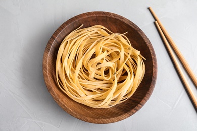 Plate of uncooked egg noodles and chopsticks on grey table, flat lay