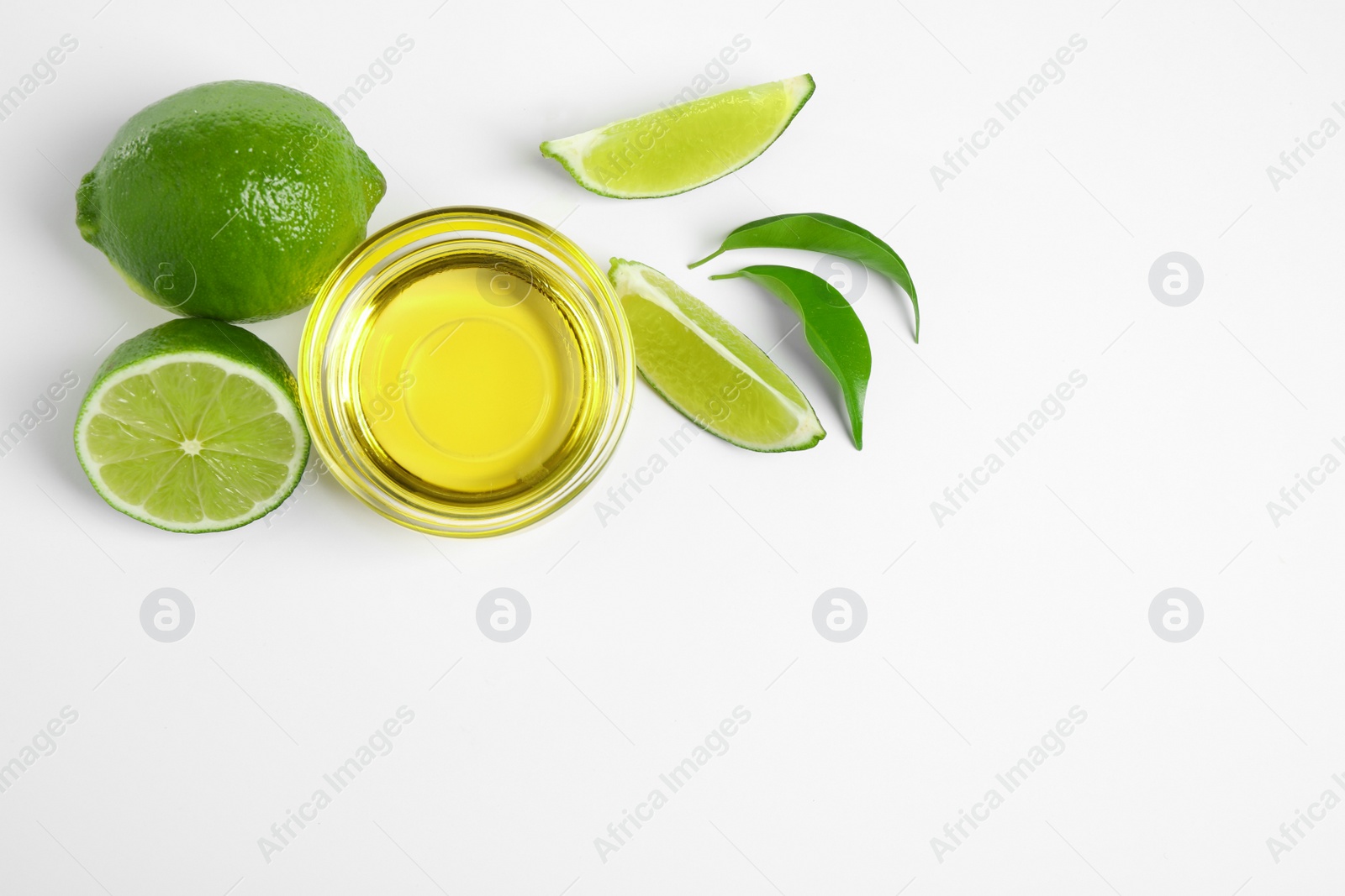 Photo of Lime essential oil in bowl and citrus fruits on white background, top view