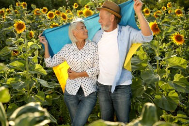 Happy mature couple with national flag of Ukraine in sunflower field