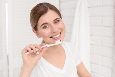 Photo of Young woman brushing her teeth indoors