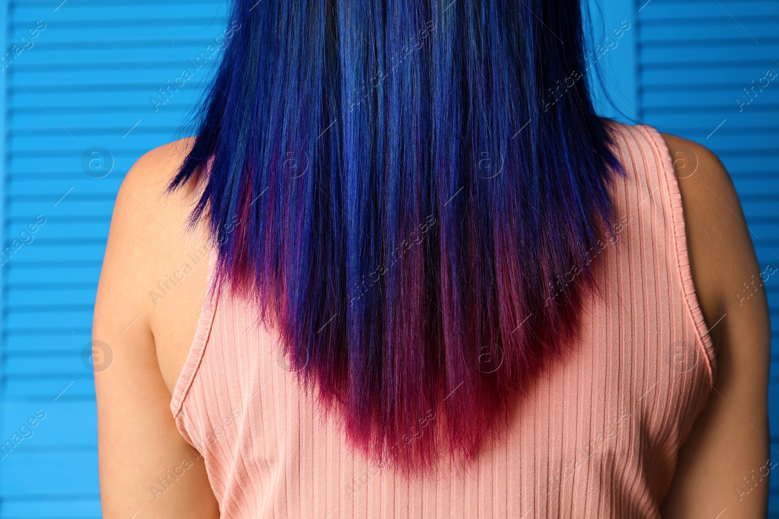 Photo of Young woman with bright dyed hair on blue wooden background, back view. Closeup