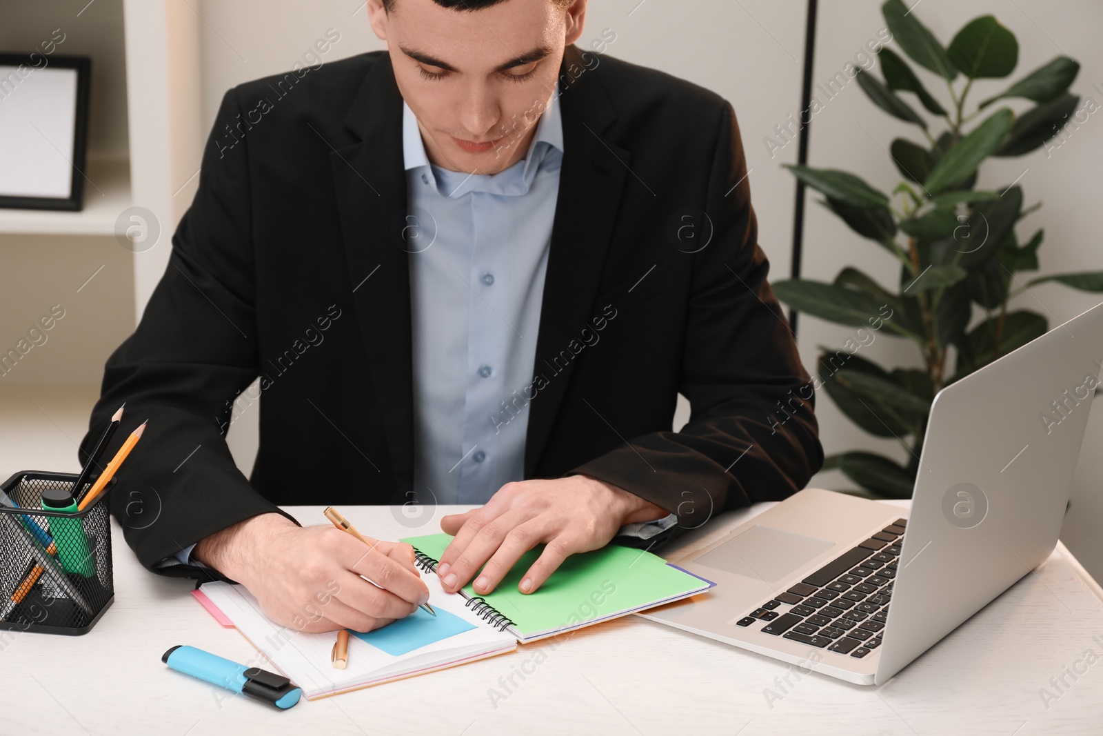 Photo of Man taking notes at white wooden table in office