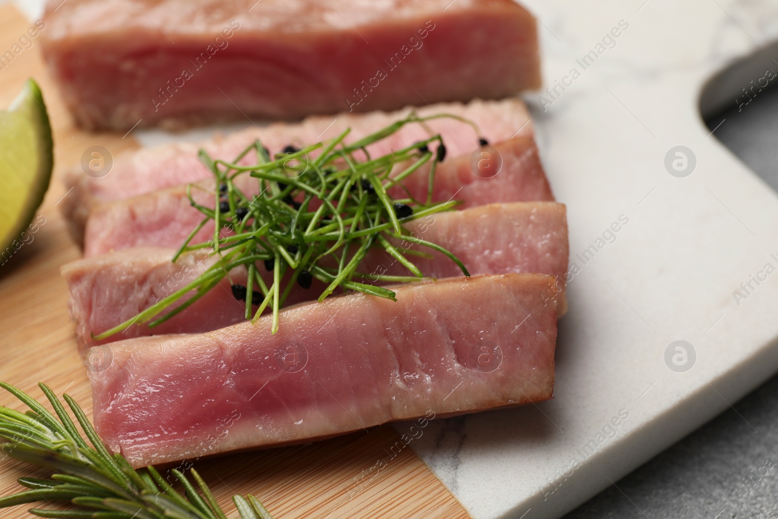 Photo of Pieces of delicious tuna steak with microgreens and rosemary on board, closeup