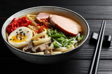 Delicious ramen in bowl and chopsticks on black wooden table, closeup. Noodle soup