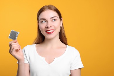 Photo of Woman holding condom on yellow background, space for text. Safe sex