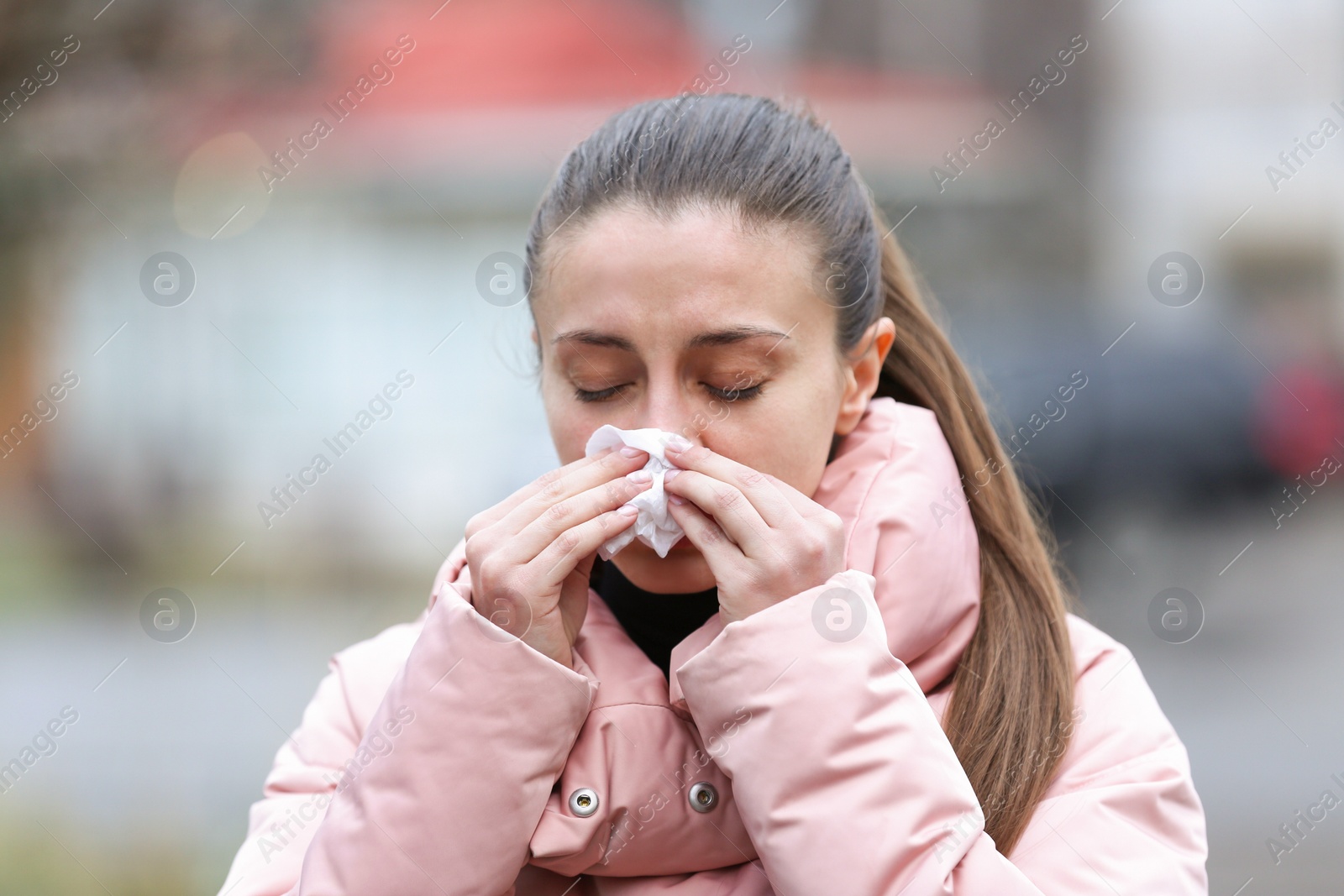 Photo of Ill woman with paper tissue sneezing outdoors