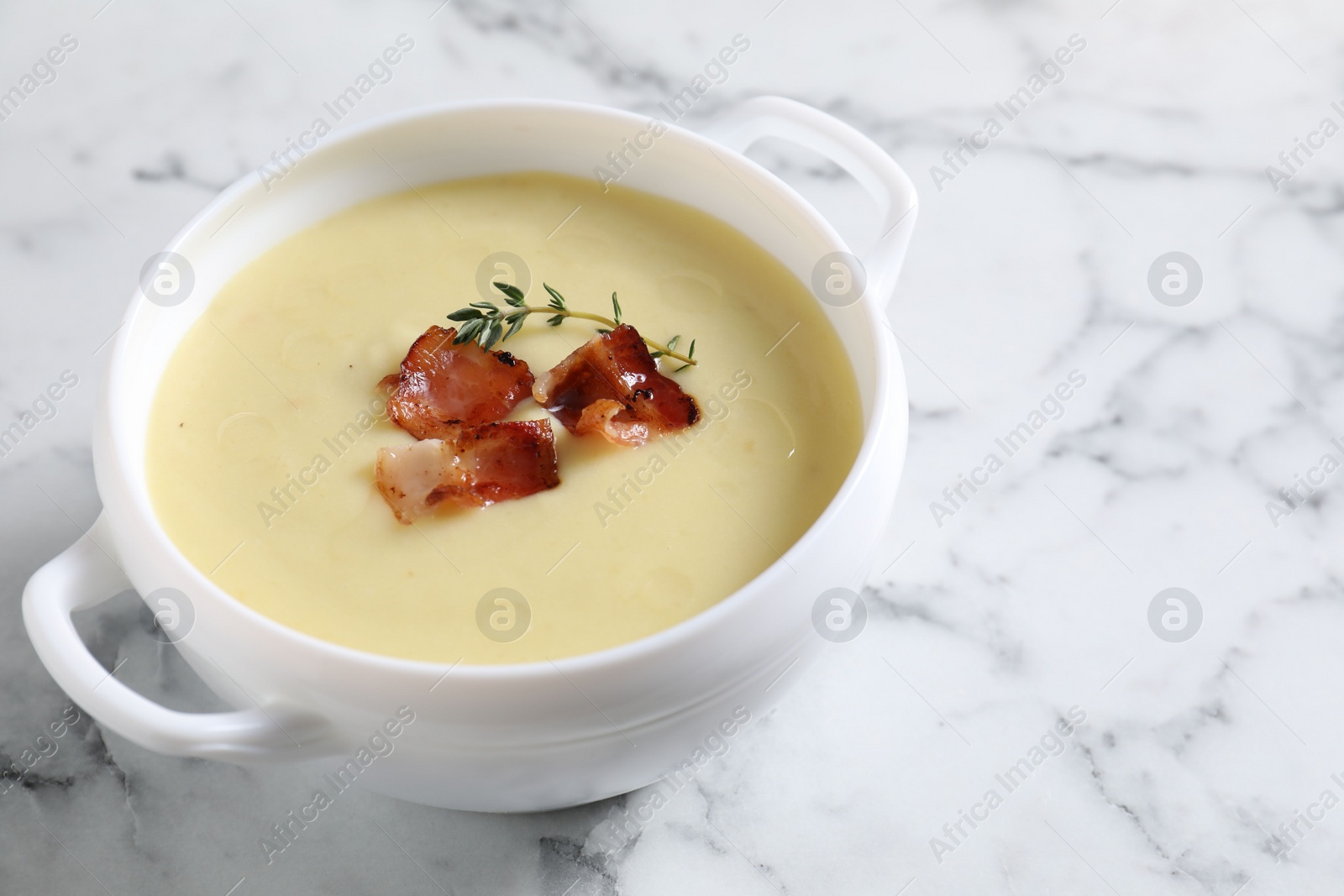 Photo of Tasty potato soup with bacon and rosemary in bowl on white marble table, closeup. Space for text