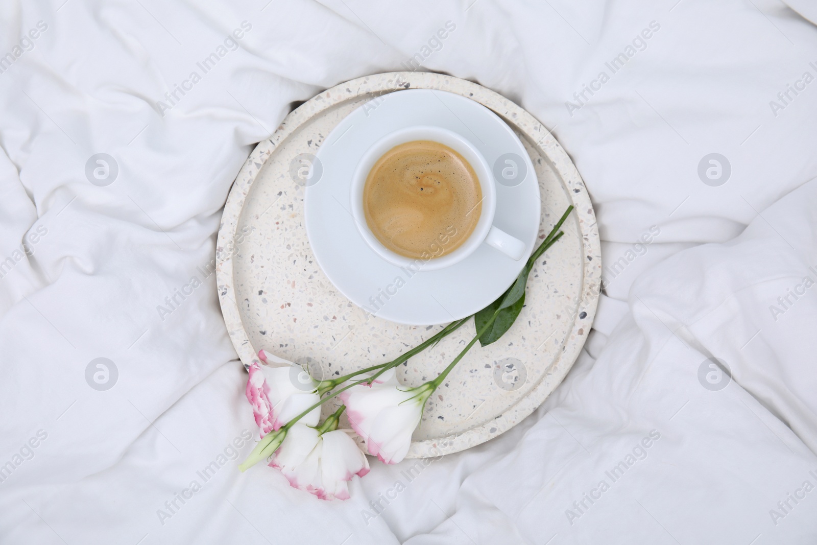 Photo of Tray with cup of coffee and flowers on white bed, top view