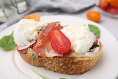 Delicious sandwich with burrata cheese, ham, radish and tomato on plate, closeup