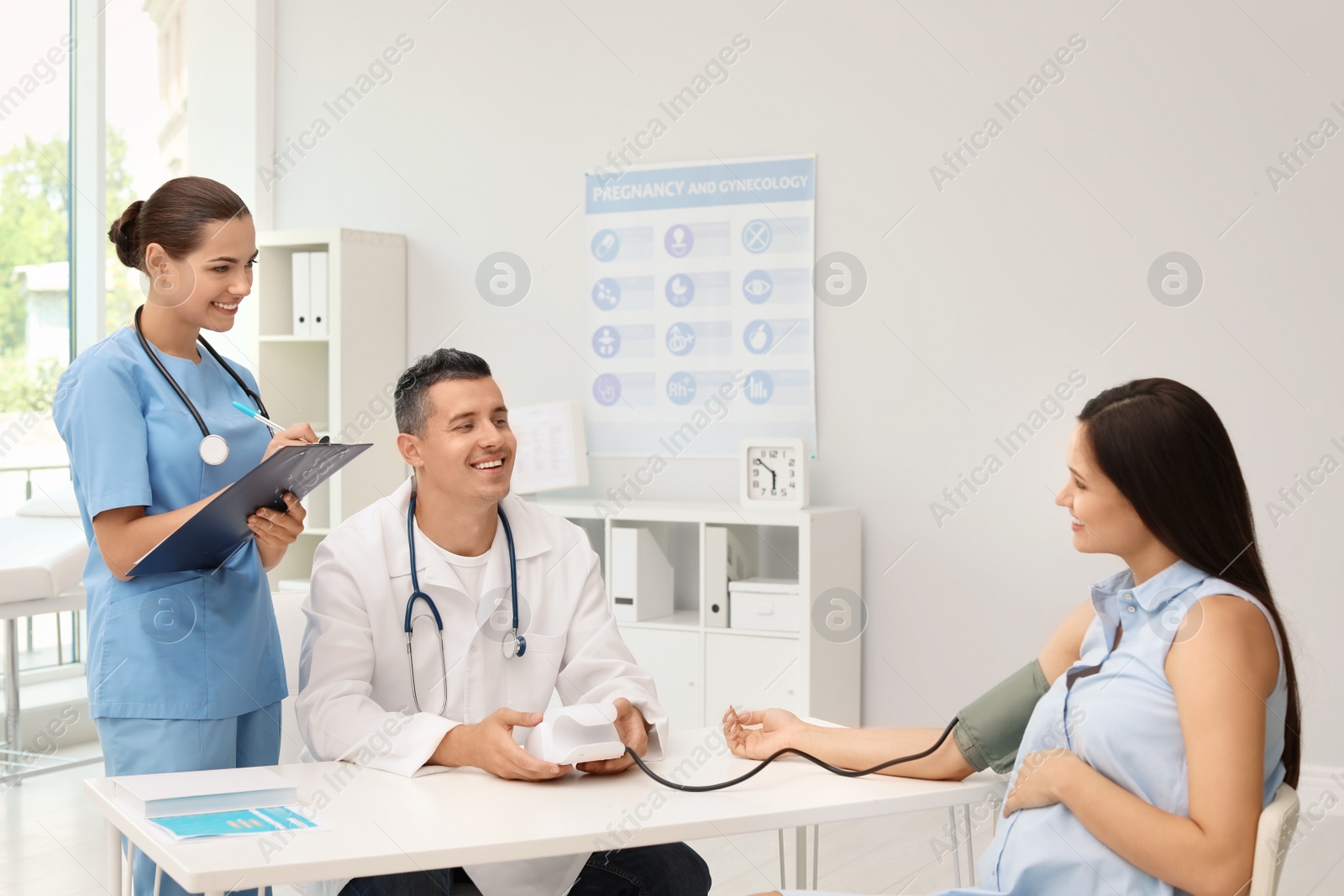 Photo of Doctor and his assistant checking pregnant woman's blood pressure in hospital. Patient consultation