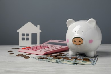 Piggy bank, house model, calculator and money on white wooden table