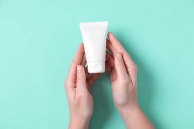 Woman with tube of hand cream on turquoise background, top view