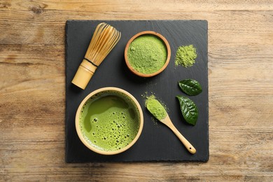Cup of fresh matcha tea, green powder and bamboo whisk on wooden table, top view