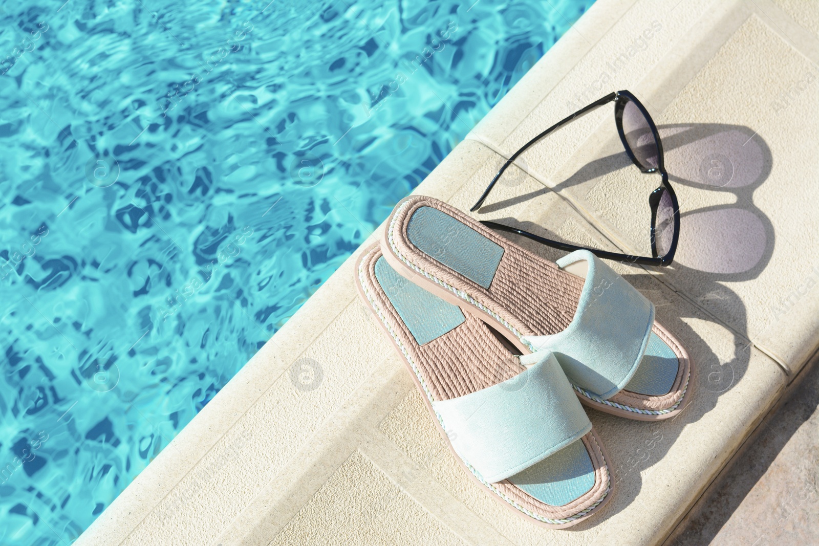 Photo of Stylish sunglasses and slippers at poolside on sunny day, space for text. Beach accessories