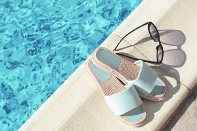 Photo of Stylish sunglasses and slippers at poolside on sunny day, space for text. Beach accessories