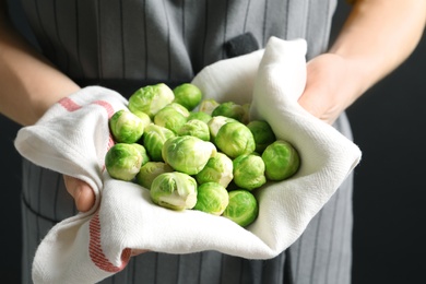 Photo of Woman holding heap of fresh Brussels sprouts in towel, closeup