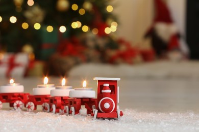 Toy train with burning candles near Christmas tree in room, closeup. Space for text