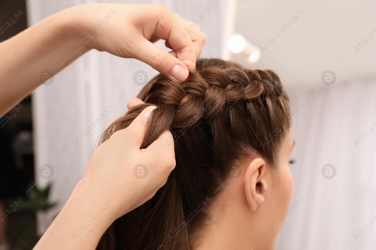 Photo of Professional stylist braiding client's hair in salon, closeup