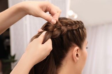 Photo of Professional stylist braiding client's hair in salon, closeup