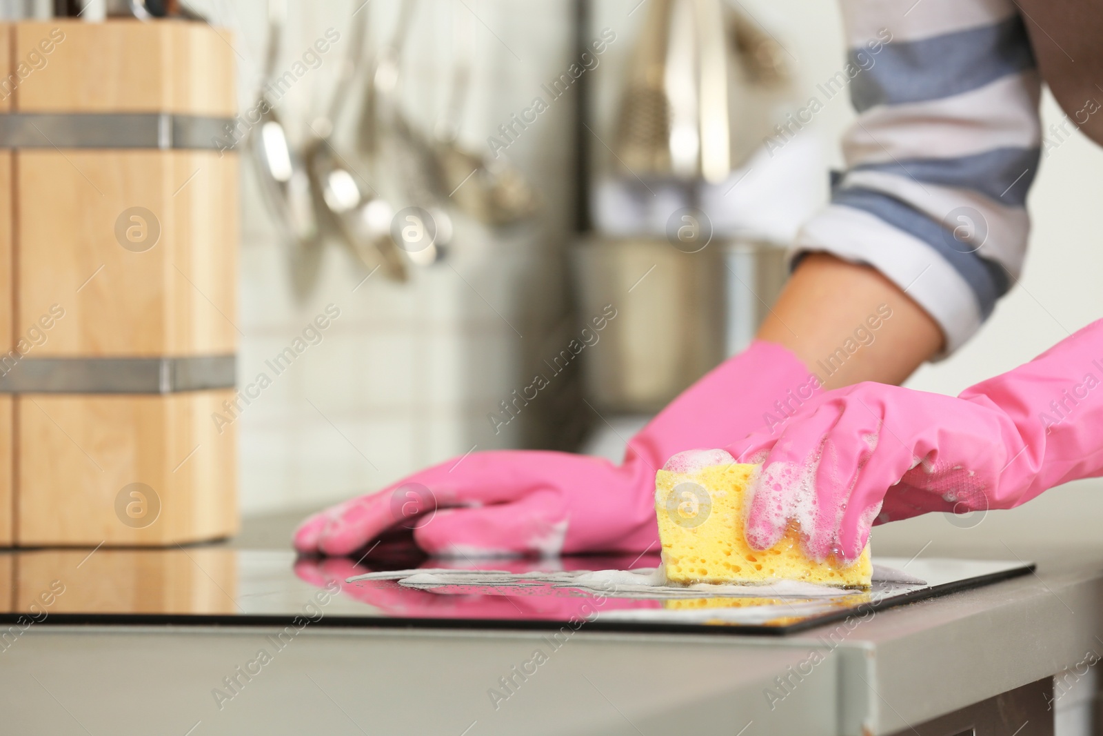 Photo of Female janitor cleaning kitchen stove with sponge, closeup. Space for text