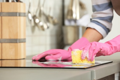 Photo of Female janitor cleaning kitchen stove with sponge, closeup. Space for text
