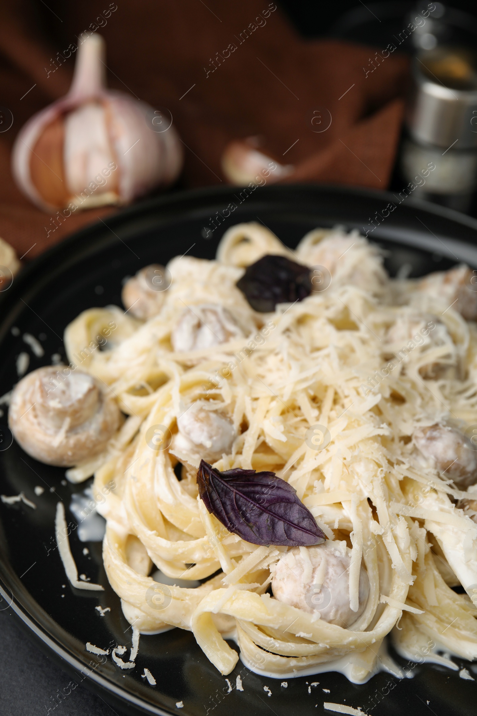 Photo of Delicious pasta with mushrooms on black plate, closeup