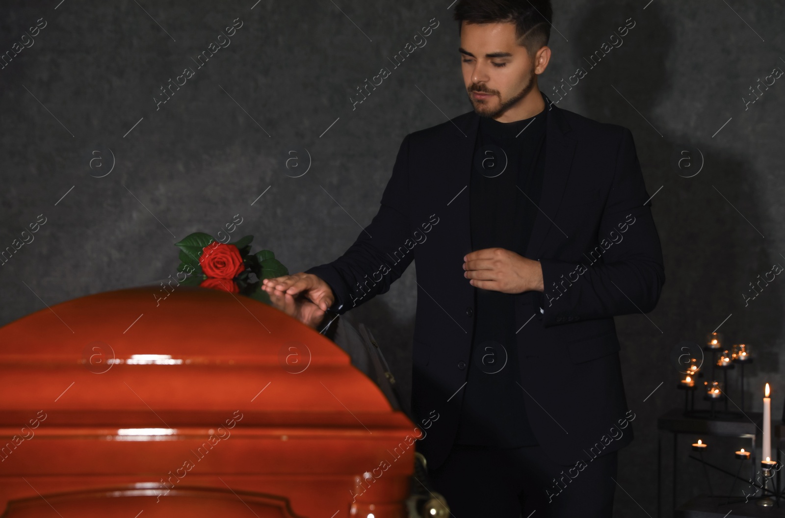 Photo of Sad young man near funeral casket with red rose in chapel