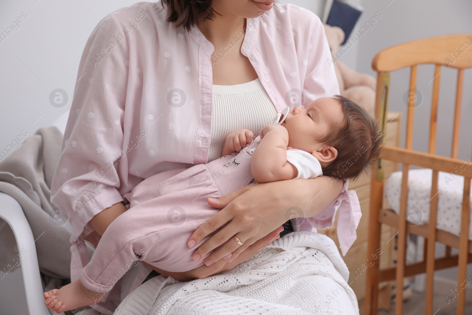 Photo of Mother holding her cute little baby with pacifier at home, closeup