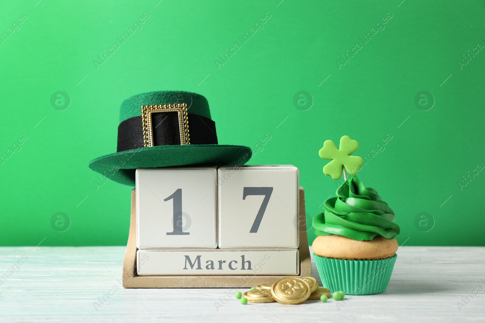 Photo of Decorated cupcake, wooden block calendar, hat and coins on white table. St. Patrick's Day celebration