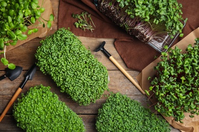 Fresh organic microgreens and gardening tools on wooden table, flat lay