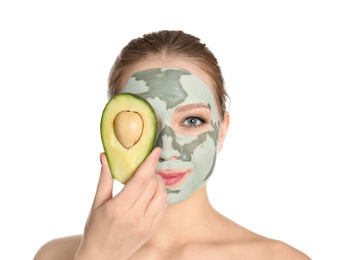 Beautiful woman holding avocado near her face with clay mask on white background