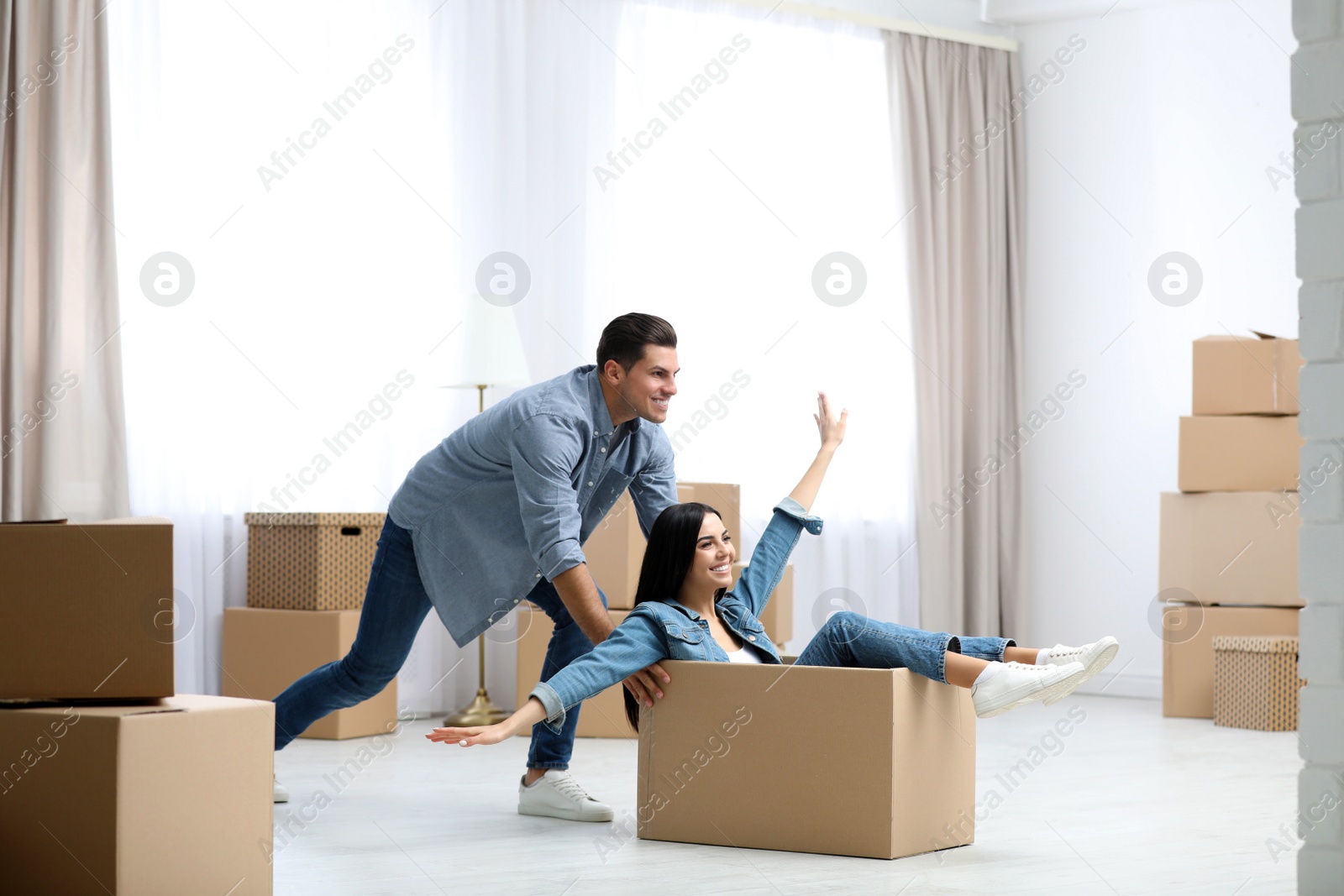 Photo of Happy couple having fun in room with cardboard boxes on moving day