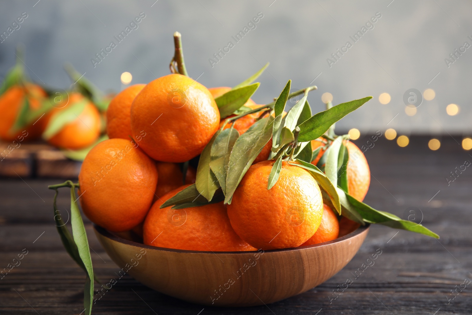 Photo of Bowl with ripe tangerines and blurred Christmas lights on background