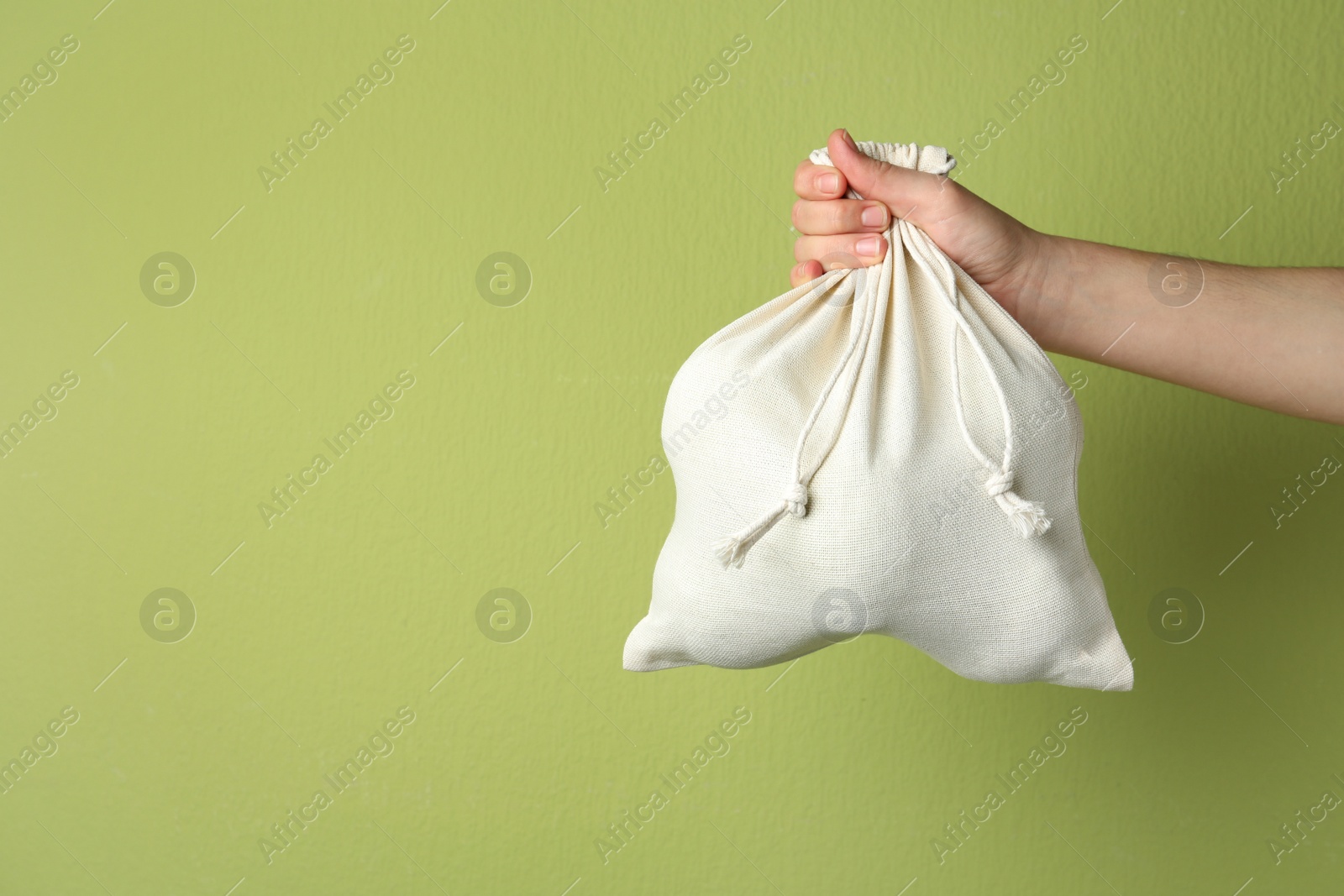 Photo of Woman holding full cotton eco bag on light green background, closeup