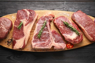 Photo of Pieces of raw beef meat and spices on black wooden table, top view